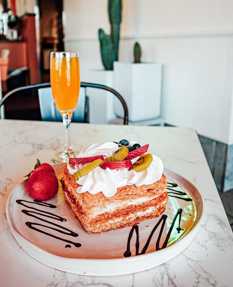 Mille-feuille pastry with whipped cream, strawberries, kiwi, and blueberries, next to a mimosa.